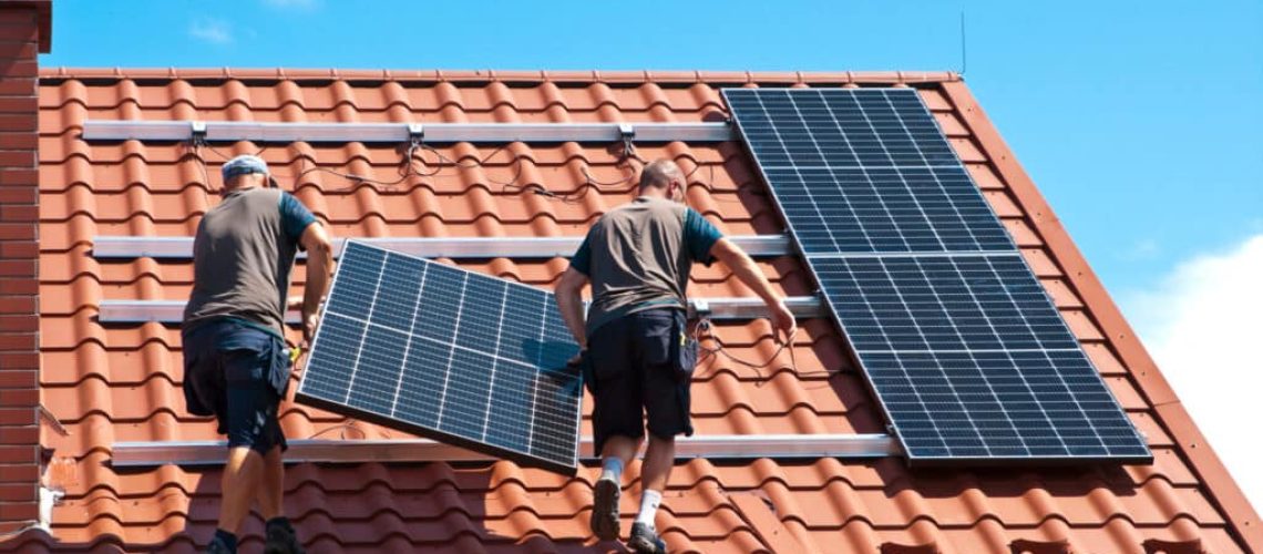 Two men installing new solar panels on the roof of a private house. Renewable energy concept and green energy abstract.